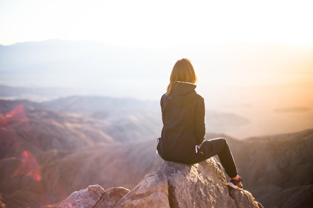image of woman sitting on mountain top, watching sunrise, thinking