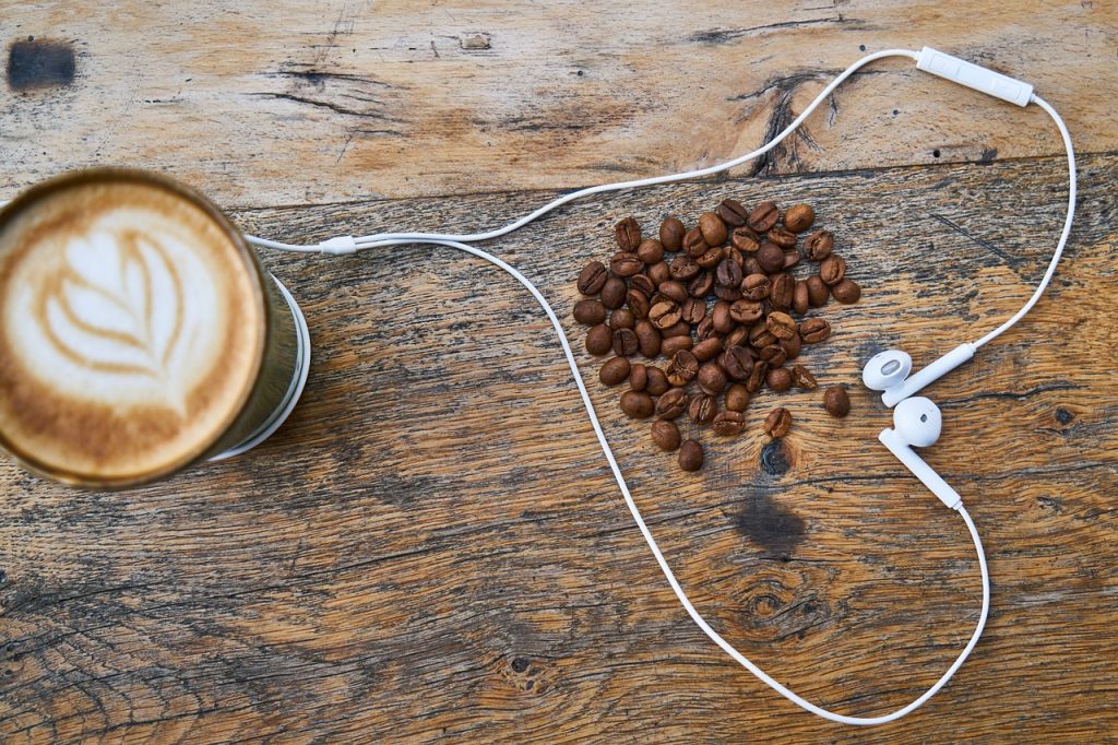 mug of coffee with heart design, coffee beans surrounded by ear plugs in heart shape, old wooden table - brown 