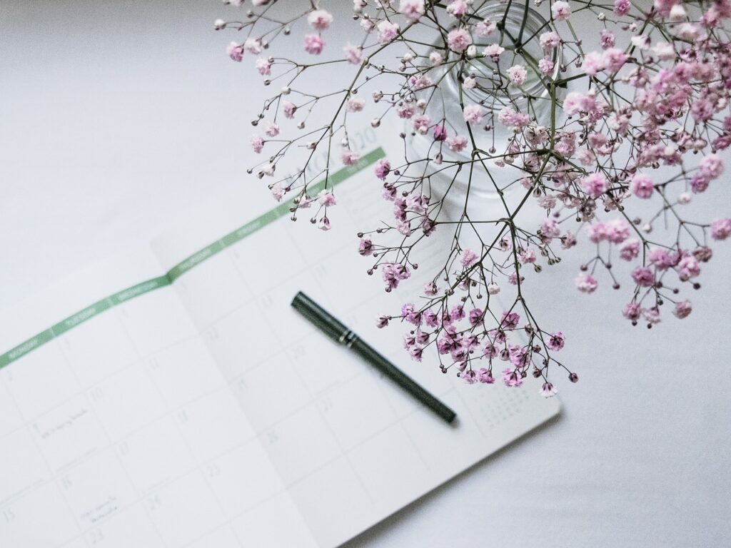 planner w-flowers white background image with planner, black pen, and pink baby's breath bouquet