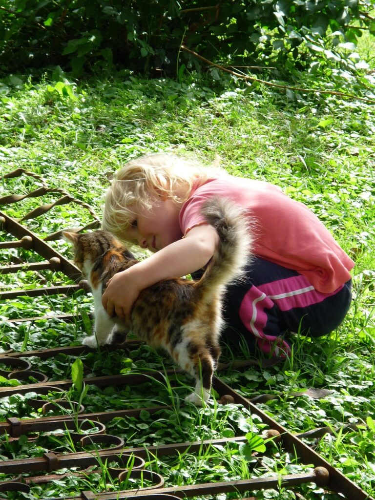 child with cat child playing outside and petting a cat